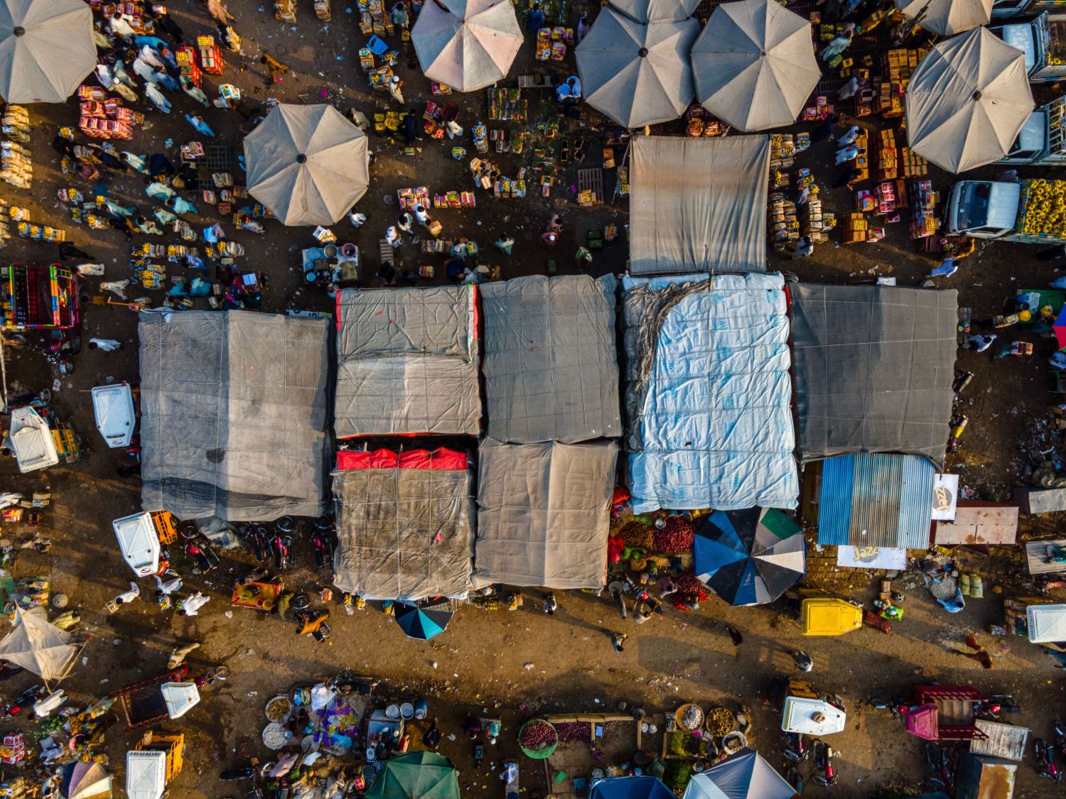Aerial view of a busy open-air market with stalls, umbrellas and delivery vehicles